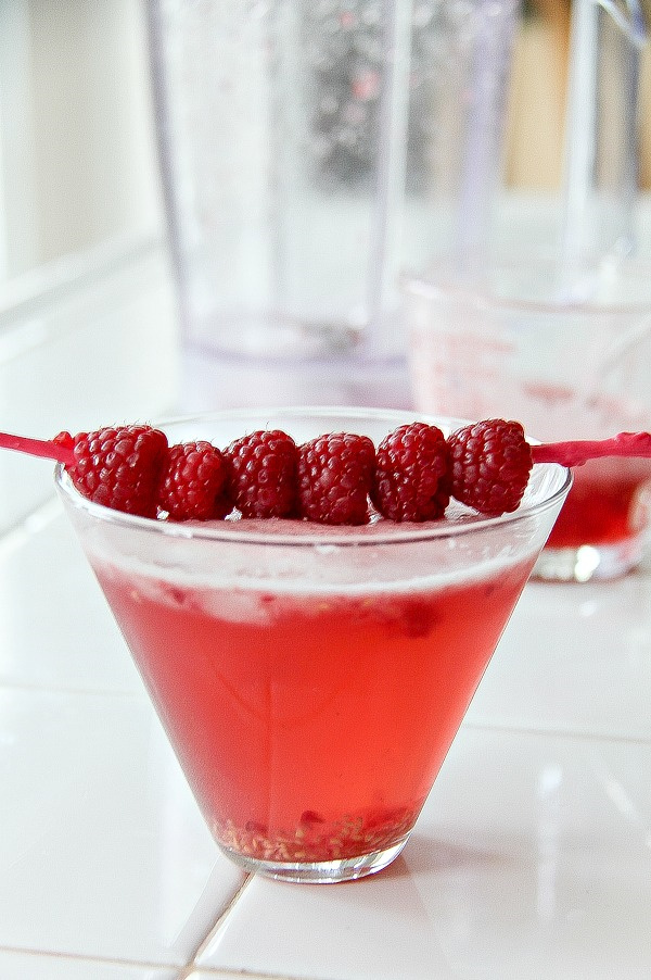 raspberries on a stick placed on top of a red cocktail