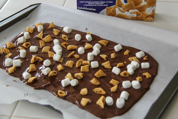 melted chocolate spread on parchment paper on a tray with marshmallows and cereal sprinkled on top