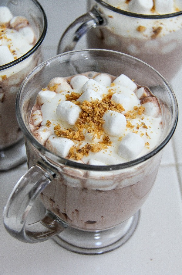 hot chocolate in a clear mug topped with marshmallows and graham crackers
