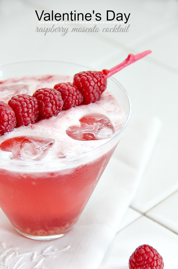 a pink cocktail with heart shaped ice cubes and raspberries on top