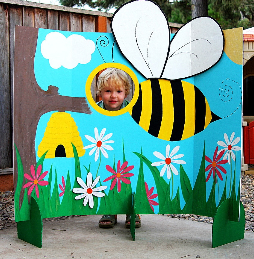 a tri-fold board painted with flowers and a giant bee with a hole cut out for photos