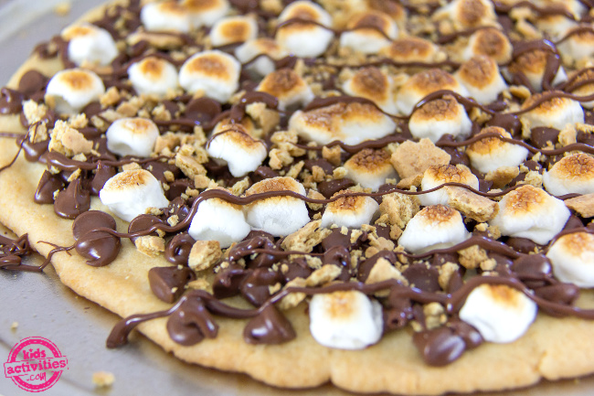 a s'mores cookie pizza topped with chocolate morsels, mini marshmallows, and crushed graham crackers
