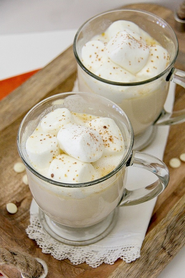 an alcoholic white hot chocolate in a clear glass with marshmallows and cinnamon on top