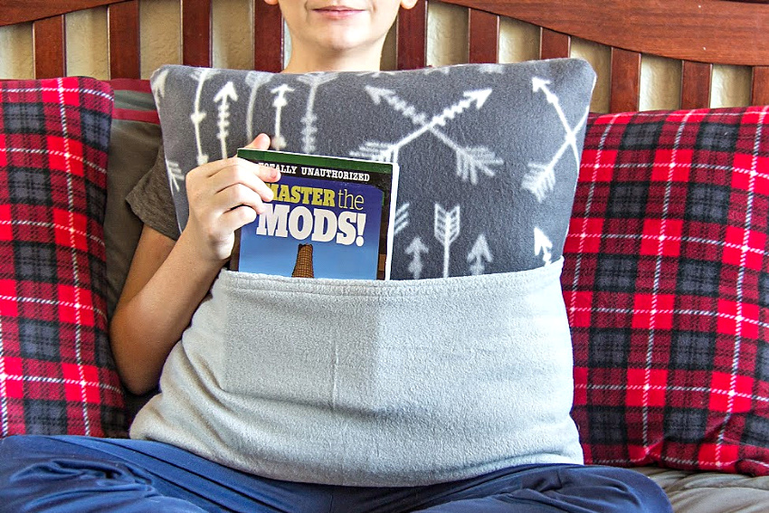 a boy sitting on a bed holding a fleece book pillow