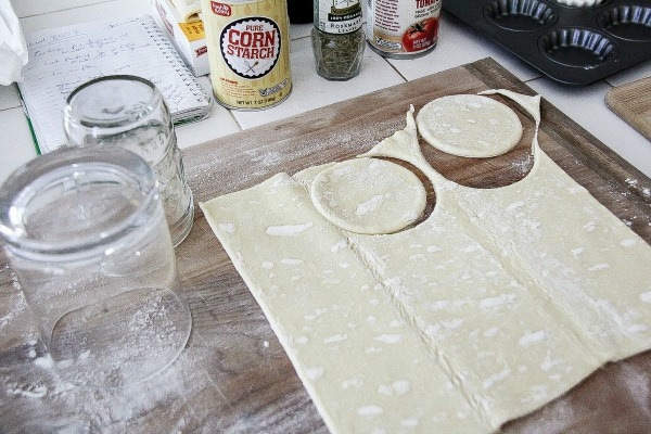a glass and glass jar being used to cut circles out of puff pastry