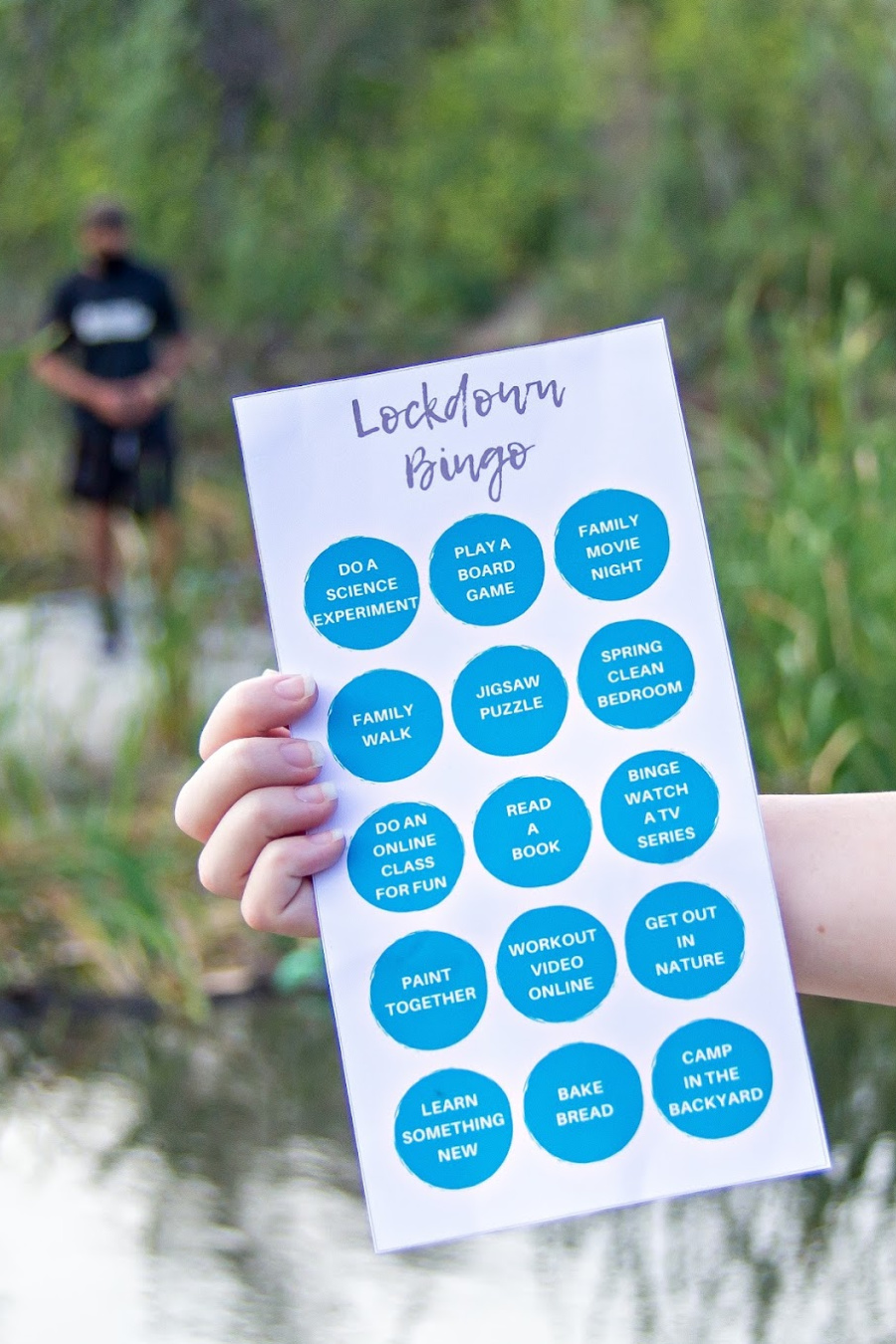 a hand holding a lockdown bingo card out in nature