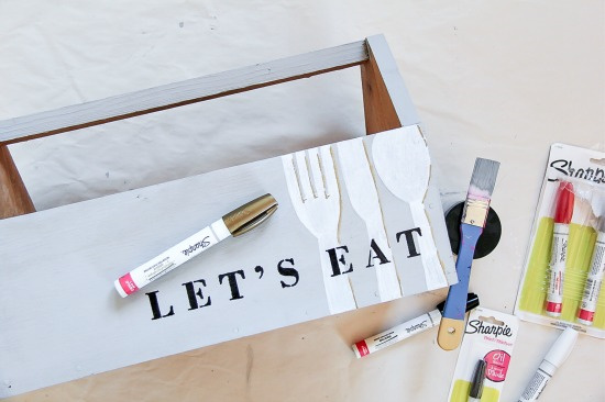 sharpie paint markers being used to paint let's eat and utensils on a wood caddy