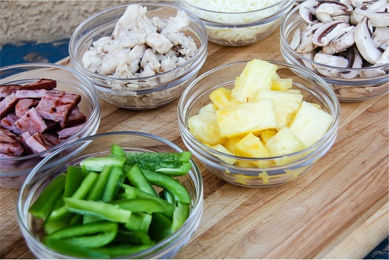 individual bowls filled with pizza toppings such as green peppers, pineapple, grilled ham, mushrooms, and chicken.