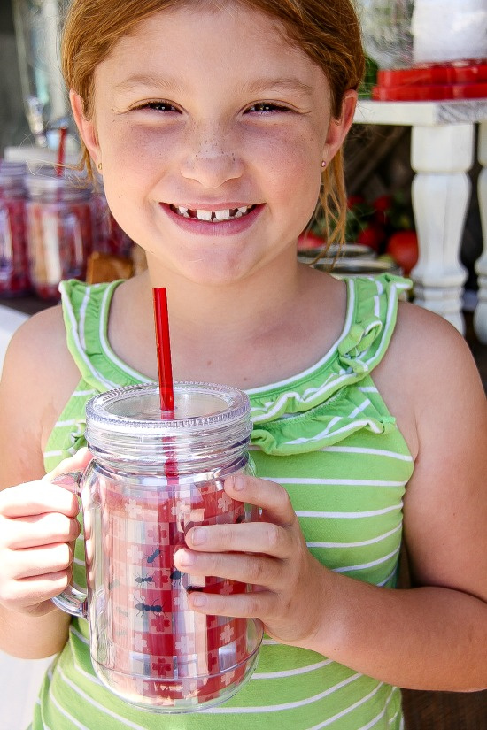 a girl holding a picnic themed cup with a straw that looks like a picnic blanket with ants crawling on it