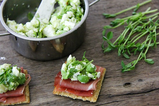 crackers topped with prosciutto, peas, feta cheese, and greens