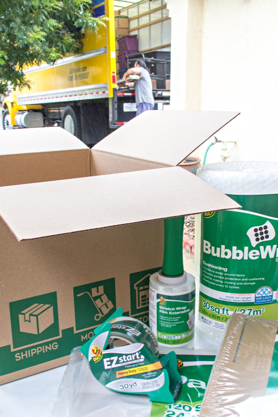 a yellow moving truck with a table and Duck Brand packing and moving supplies in front of it