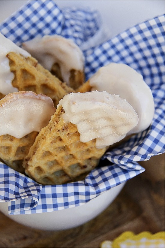 waffle sticks dipped in icing and cinnamon sugar in brown and white checked parchment paper in a white bowl