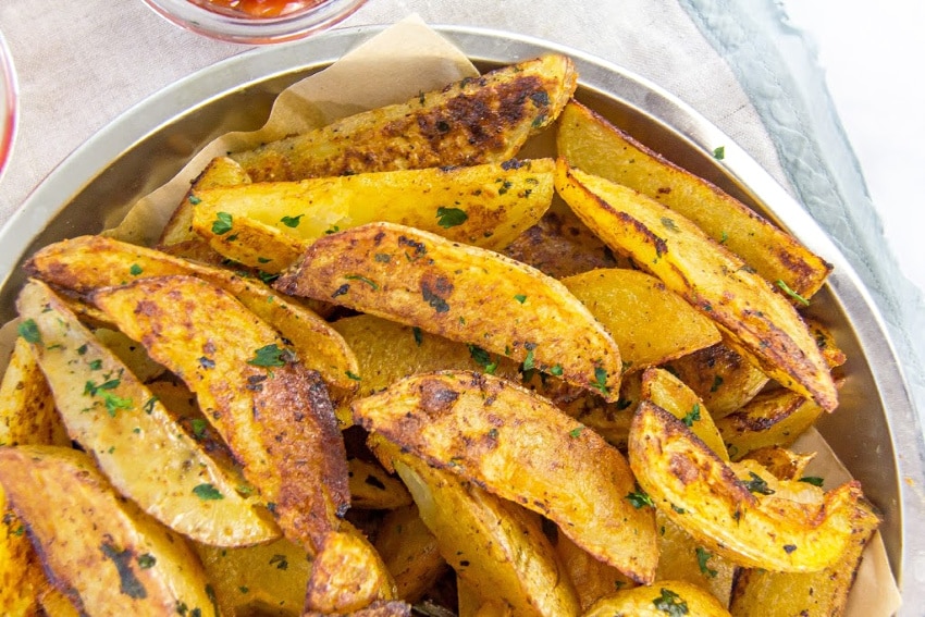 seasoned potato wedges in a silver tray with parchment paper