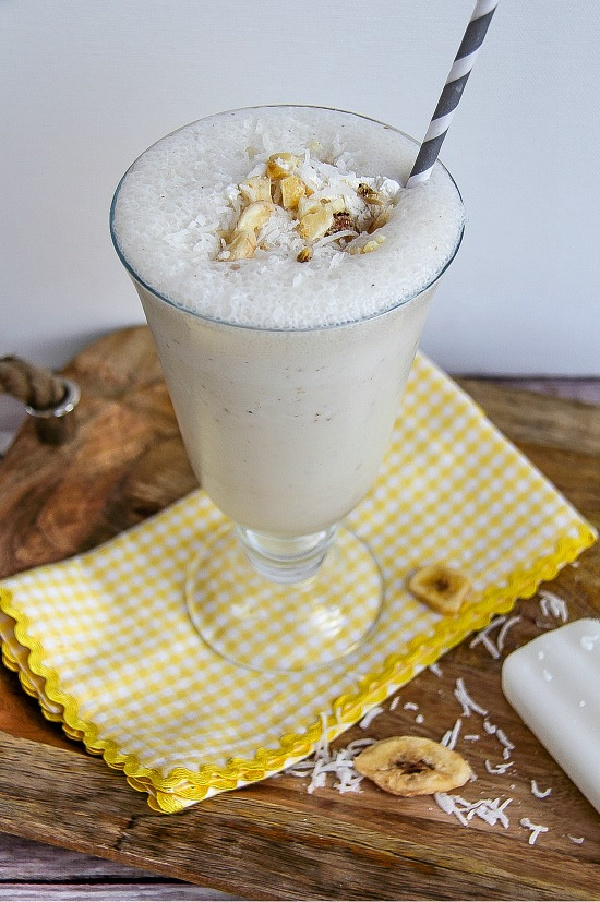 a banana coconut shake in a milkshake glass topped with chopped dried banana and coconut flakes