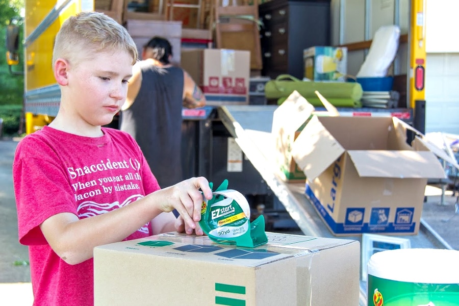 a child and man packing boxes and loading household belongings onto a moving truck