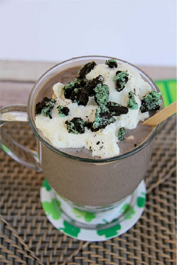 a hot chocolate in a clear mug topped with whipped cream and crushed mint Oreo's.