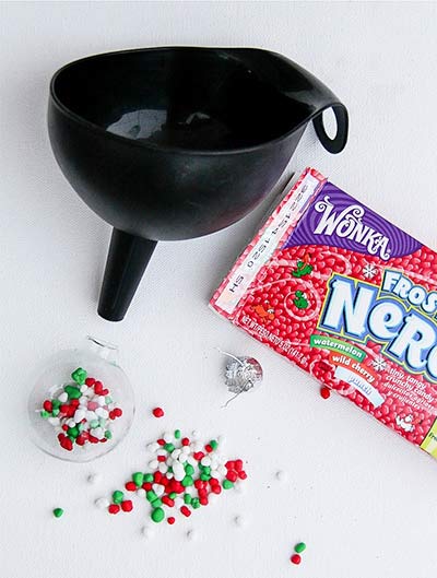 a funnel being used to put Wonka Nerds inside clear christmas ornaments