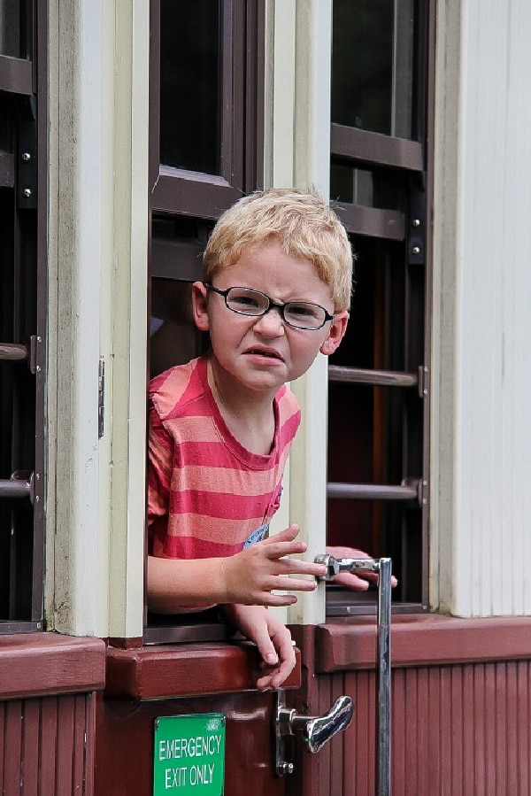 a boy pulling a face while hanging out the window of a train