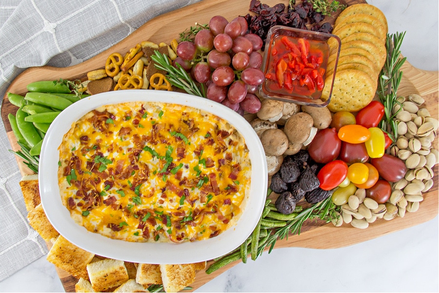 Kentucky Hot Brown dip on a holiday charcuterie board with tomatoes, crackers, Texas Toast squares, fruit, and pistacchios.