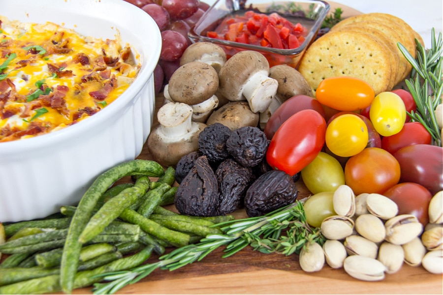 Figs, tomatoes, pistacchios, mushrooms, pimentos, and dip on a charcuterie board for the holidays.