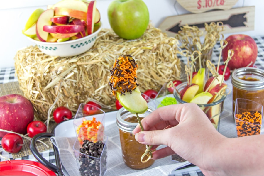 A caramel apple dipping party table for the whole family including toppings, apple slices, and caramel sauce.