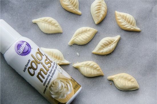 white chocolate leaves being sprayed with edible gold spray to make gold wings