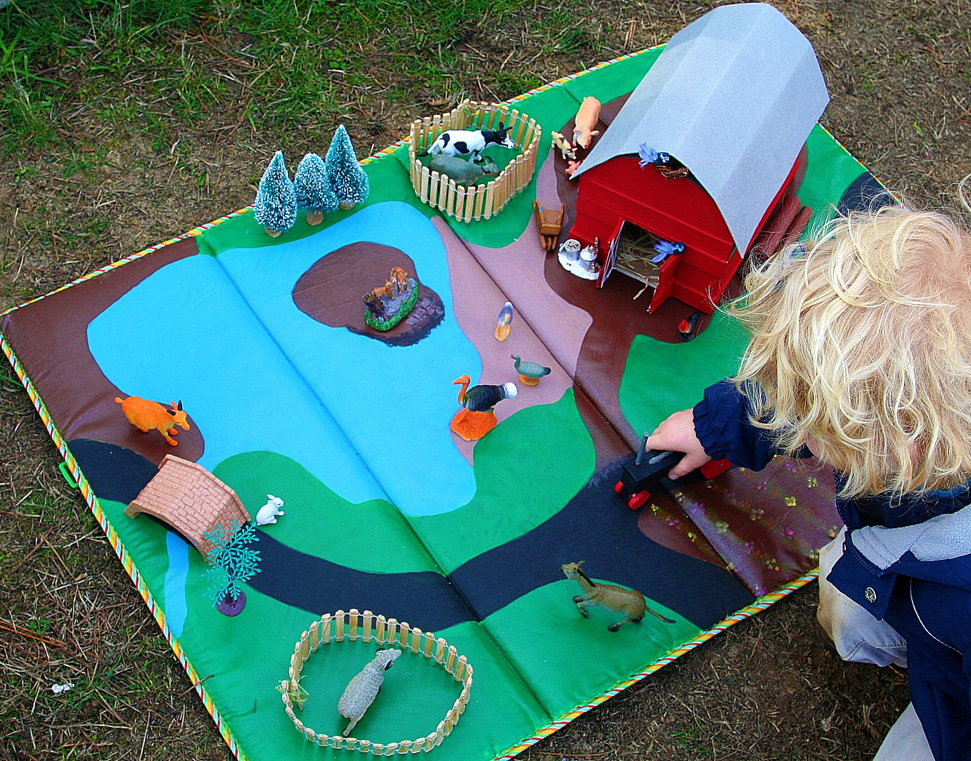 A boy playing with a handmade barn on a farm play mat.