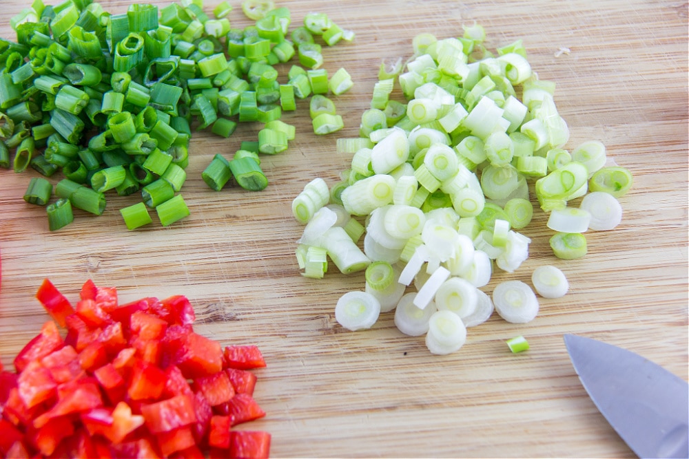 fresh red pepper and green onions sliced on a wood cutting board