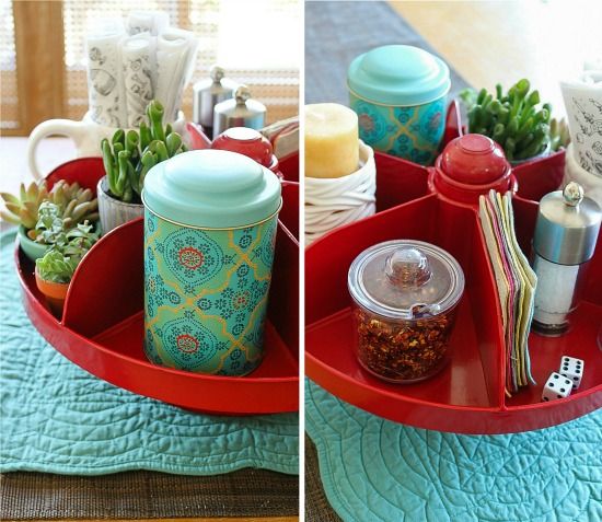 A red hardware bin on a dining table filled with candles, condiments, napkins, candles, and plants.