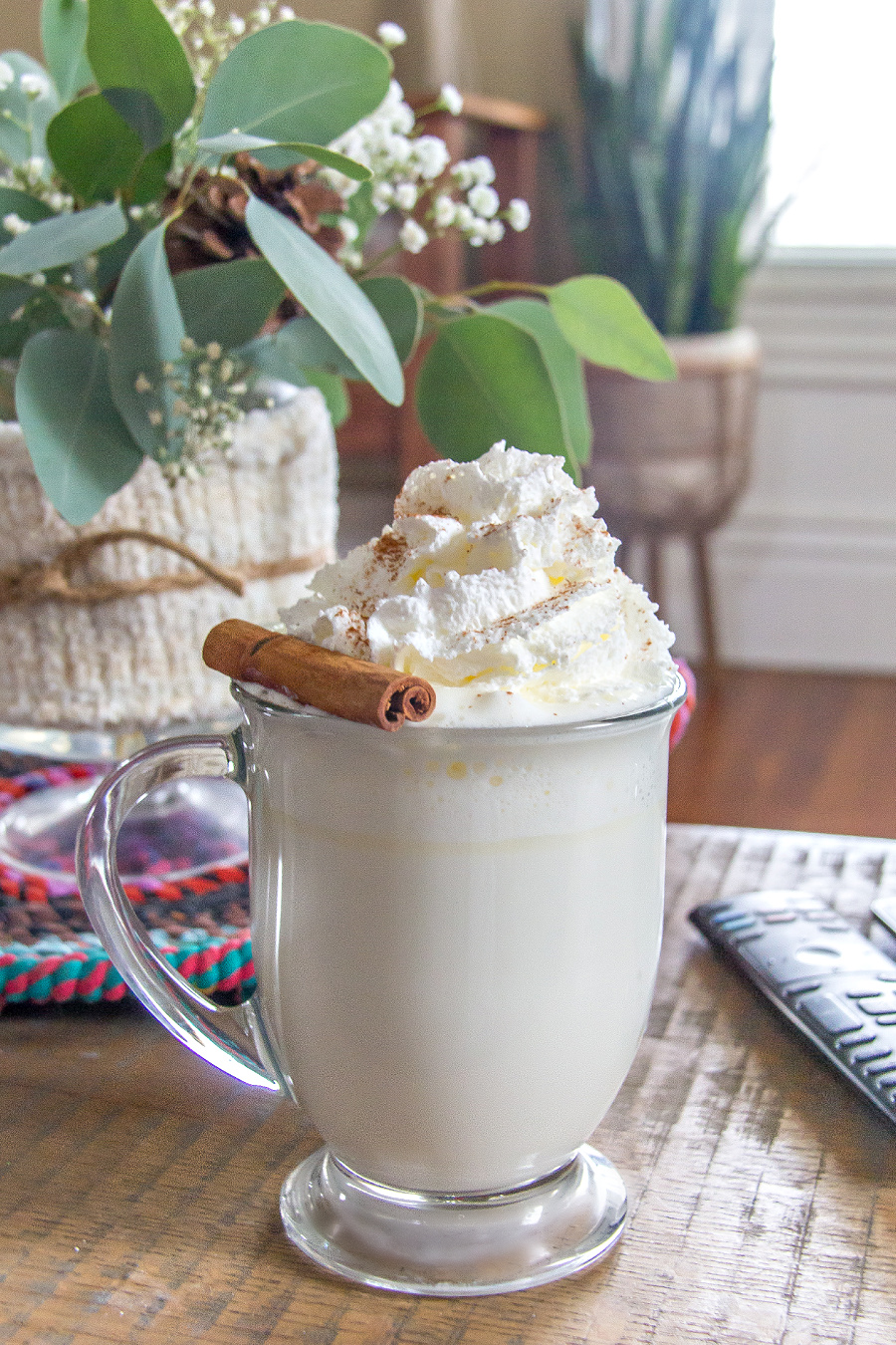 white hot chocolate topped with a cinnamon stick and ground cinnamon in a clear mug