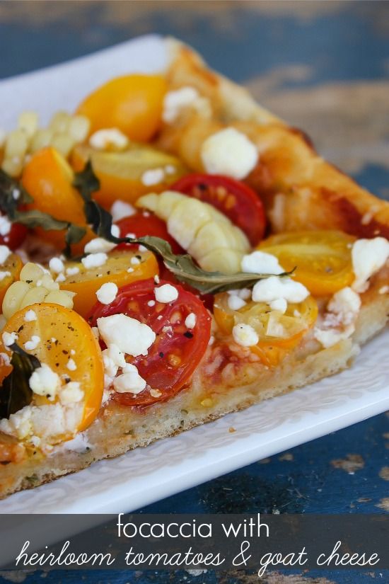 focaccia bread on a white tray topped with heirloom tomatoes, goat cheese, and corn