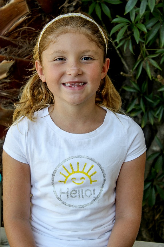 A girl wearing a white t-shirt stamped with hello sunshine.