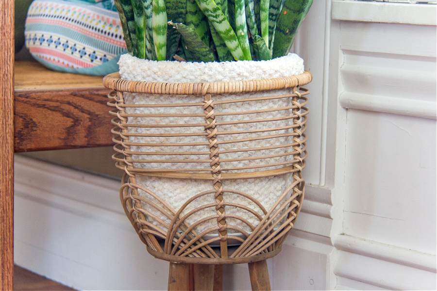 A knitted cozy for a potted plant inside a can plant stand.