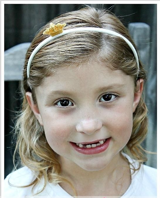 A girl wearing a white headband with a small gold crown on it.