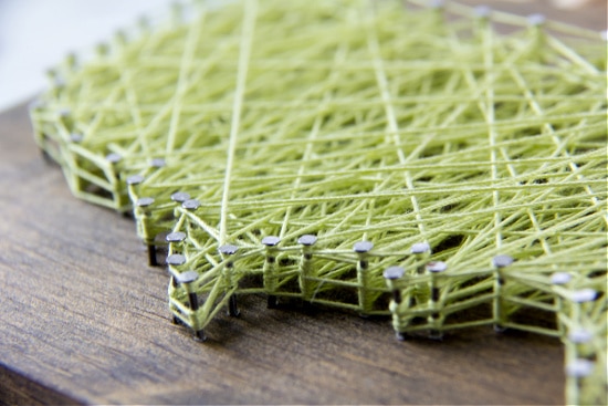 Green string wound around nails on a wood block to make string art