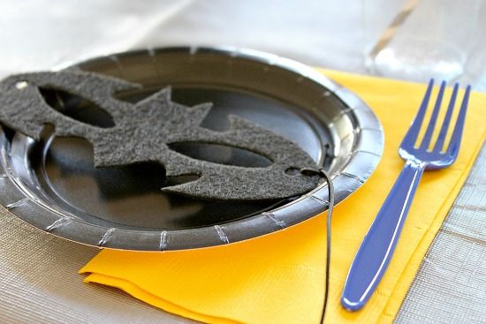 Black paper plates with yellow napkins and blue utensils for a Batman themed party. Each plate has a handmade batman mask on it.