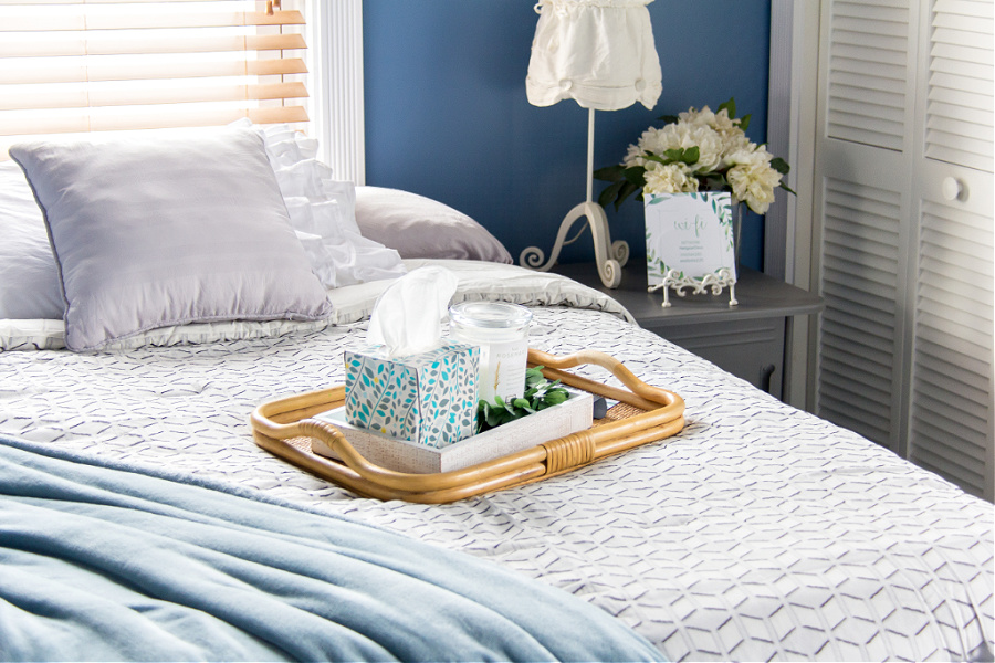 A bed with a tray that has tissues, candles, and remote controls on it in a guest bedroom