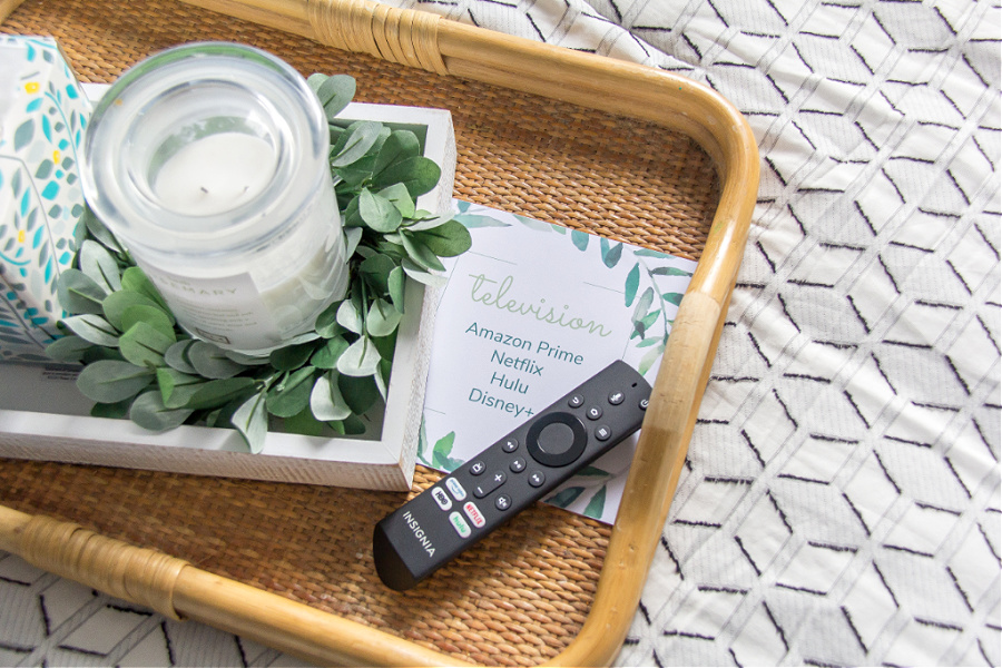 A tray on a bed with a candle, tissues, remote control and a printed card with streaming services available in a guest bedroom.