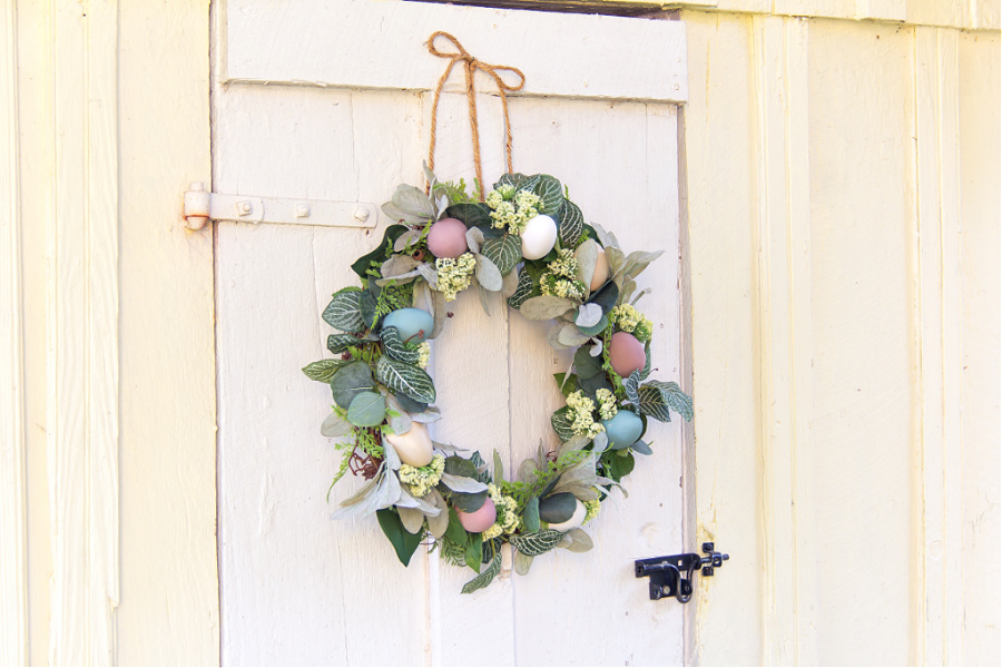 A green leaf and wood egg wreath hanging on a chicken coop door. 