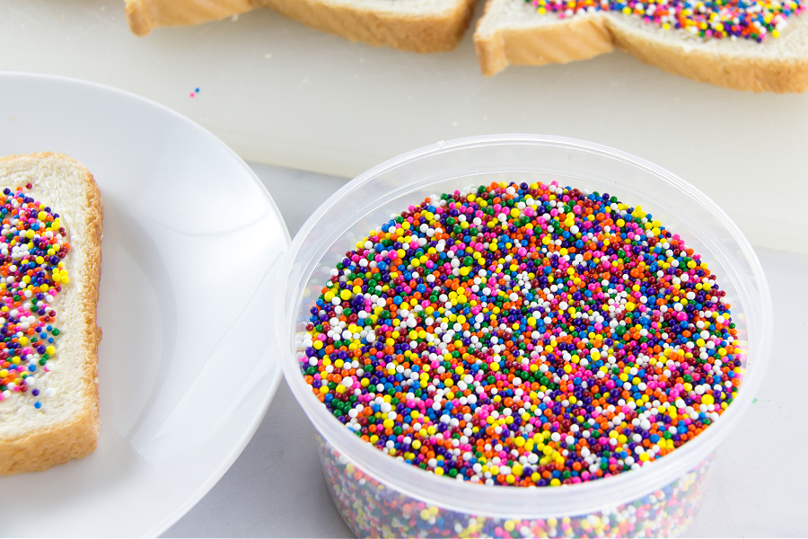 A container of hundreds and thousands next to fairy bread being made.