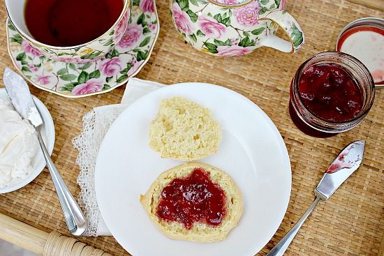 A plate of scones with homemade strawberry jam and a pot of tea.