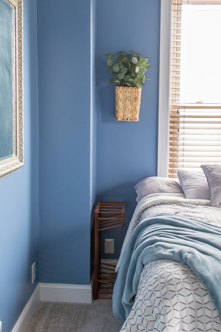 A bed with a TV dinner tray, a basket of greenery on the wall and a throw blanket in a guest bedroom.