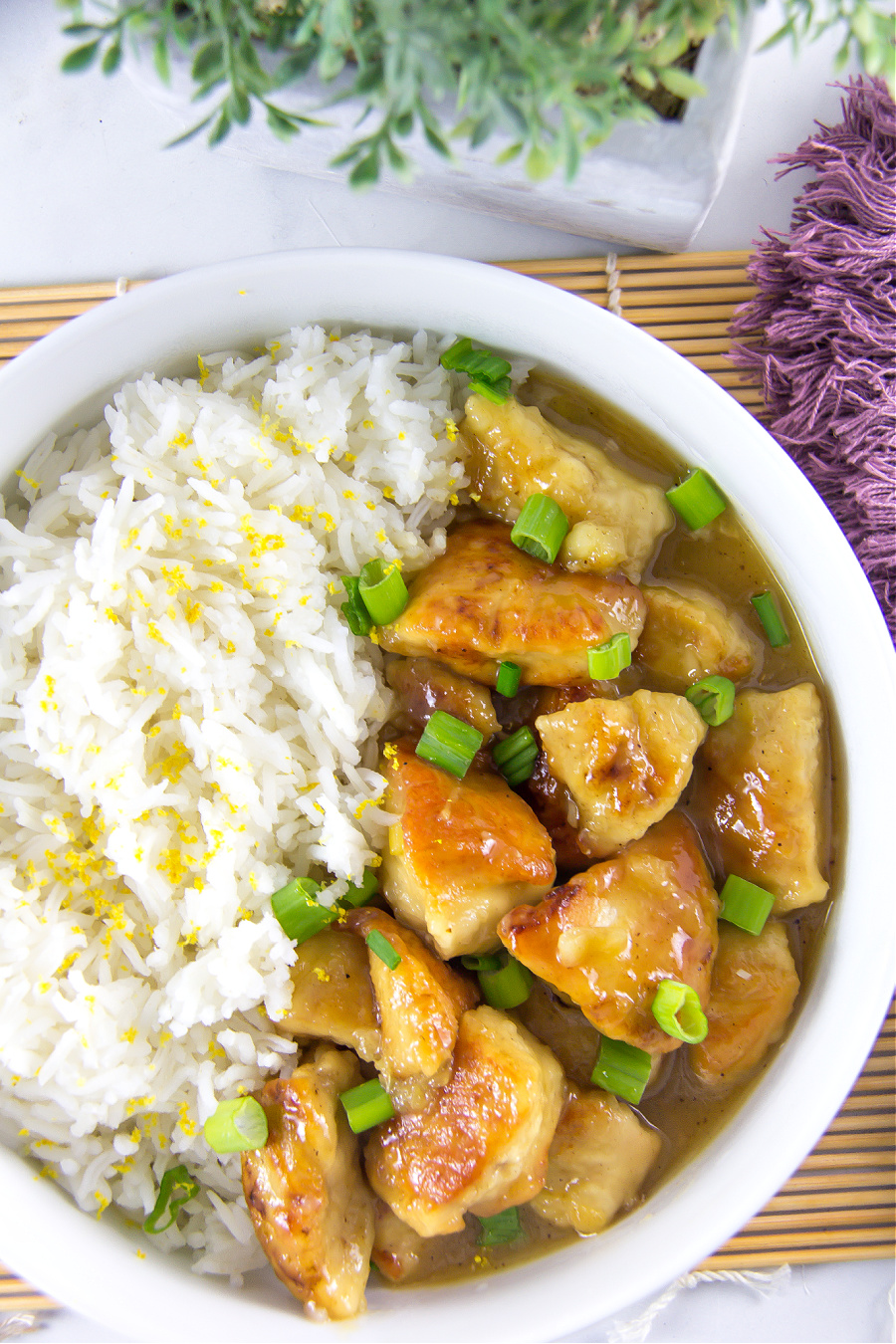 Homemade lemon chicken garnished with green onions in a bowl and served with white rice garnished with lemon rind.