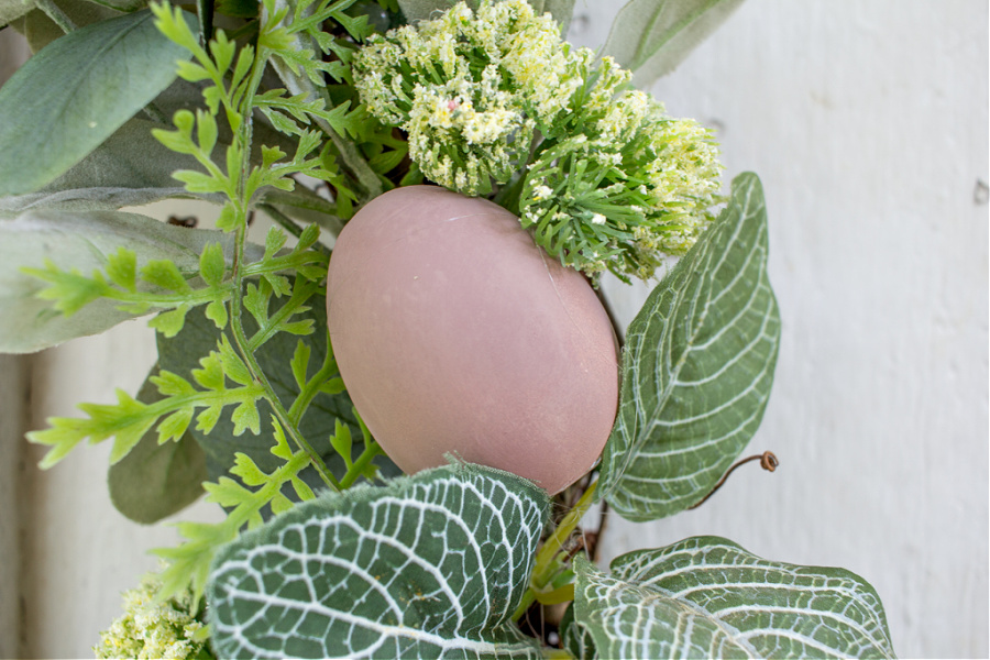 a pink wood egg painted and attached to an evergreen front door wreath