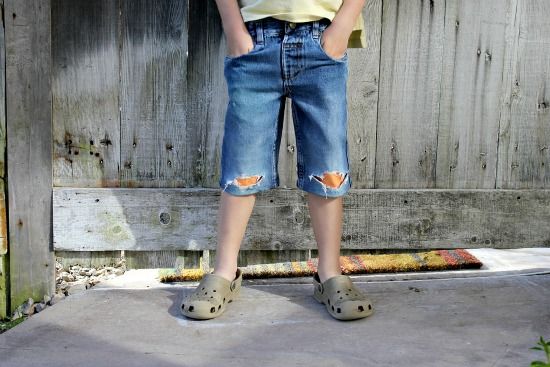 A boy wearing a pair of cut-off denim shorts with knee holes patched with orange fleece.