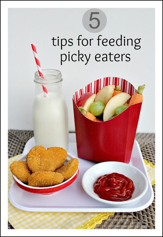 A plate of chicken nuggets with a french fry container filled with fruit and a bottle of milk next to it.