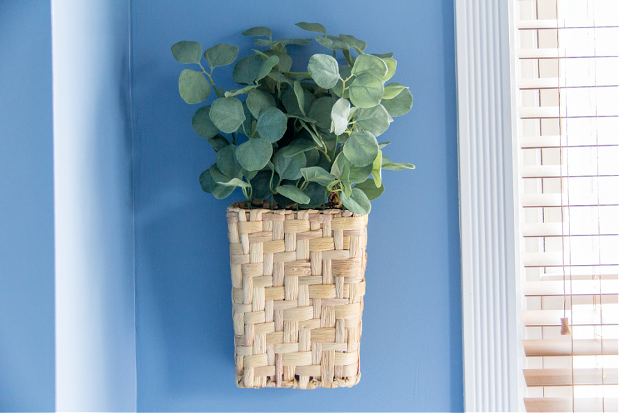 A blue bedroom wall with a basket full of greenery hanging on the wall.