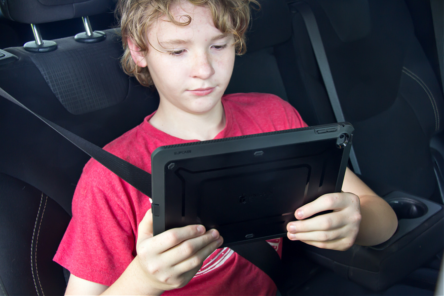 A boy in a car holding an iPad for a long road trip.