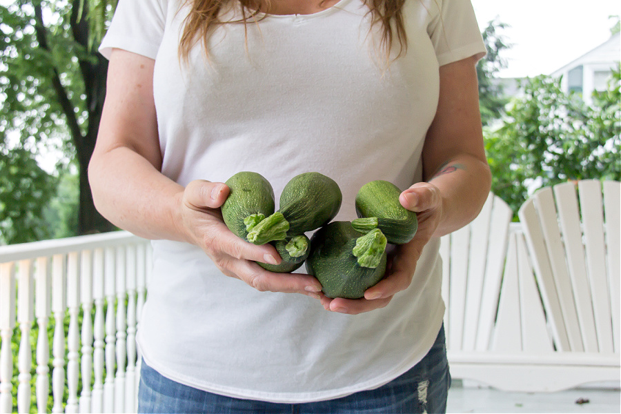 Hands holding five zucchini picked from a backyard vegetable garden.