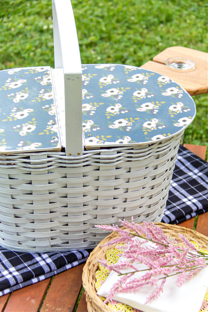 A DIY white picnic basket with a Mod Podge blue flower wood lid on top.